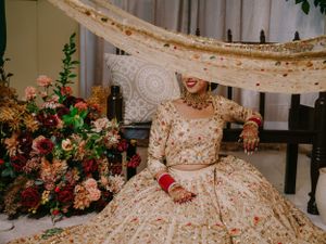 An elegant traditional wedding ensemble in cream and gold with intricate embroidery beside a lush pink floral arrangement.