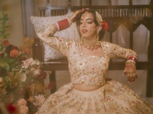A person in a traditional South Asian bridal lehenga with gold embellishments poses gracefully against a floral backdrop.