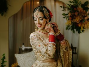 Elegant bride in traditional South Asian wedding attire with gold embroidery and red bridal jewelry smiles while getting ready.