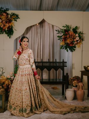 Ornate cream and gold lehenga with delicate embroidery photographed in an elegant indoor setting.