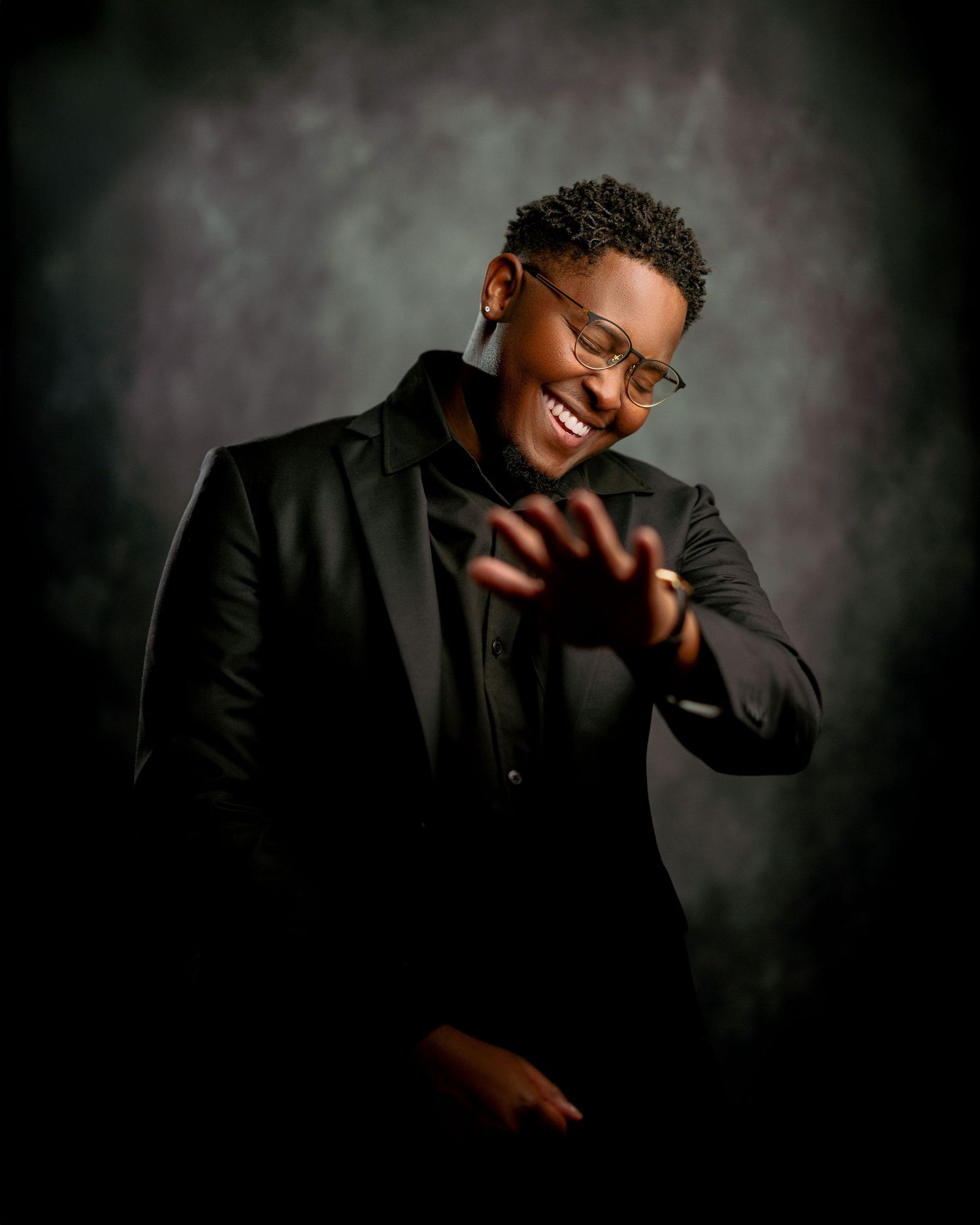 Professional studio portrait of a man in a black suit, smiling confidently against a dark, elegant backdrop