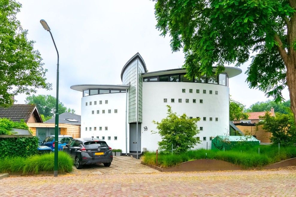 Modern white architectural building with unique design features surrounded by green trees and parked cars in front.