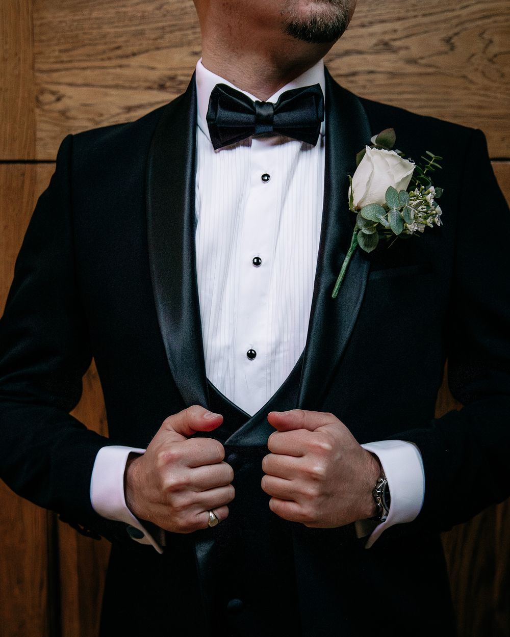 Close-up details of groom adjusting tuxedo jacket and bow tie.