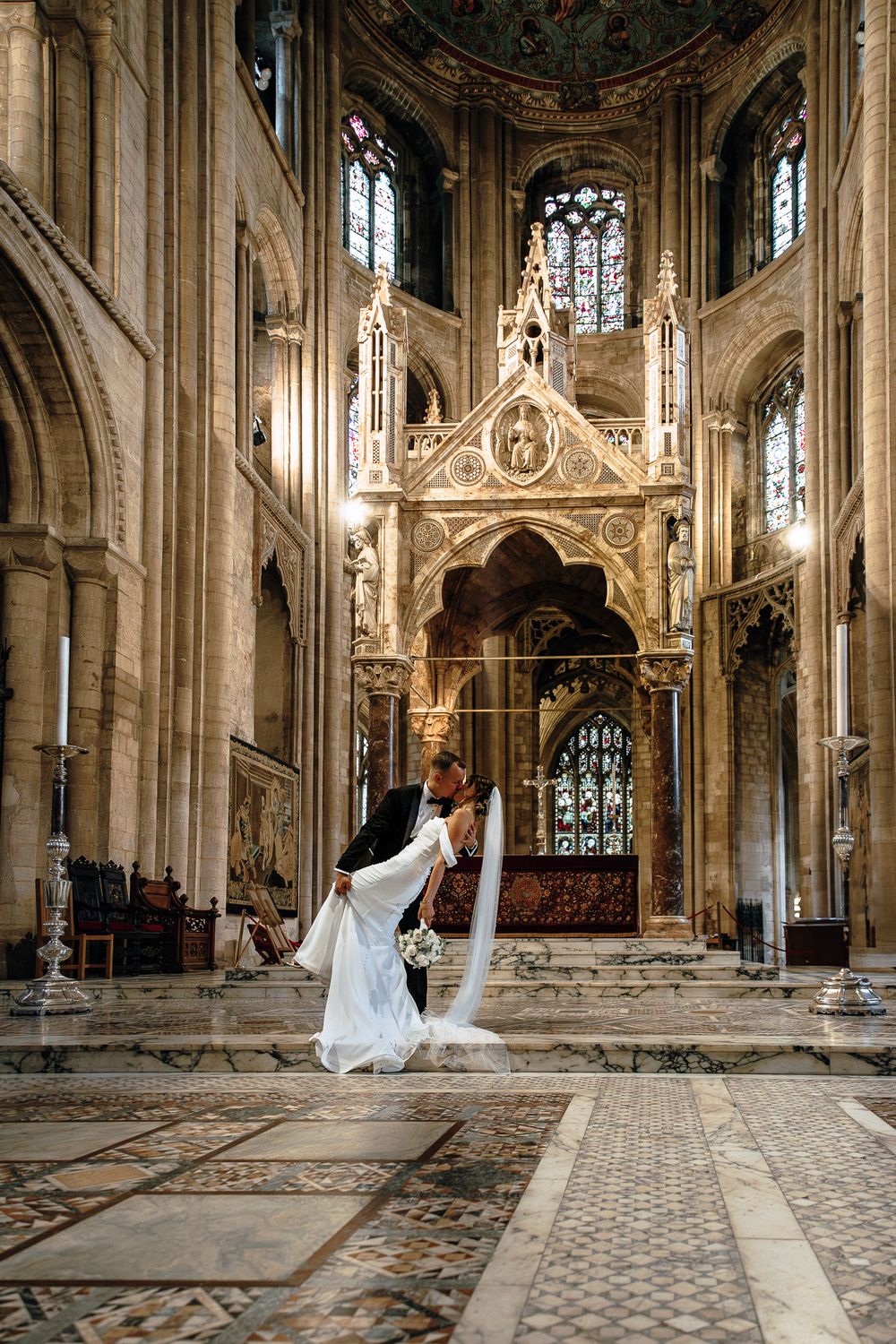 Wedding couple dancing in an ornate cathedral with stained glass windows and gothic architecture.