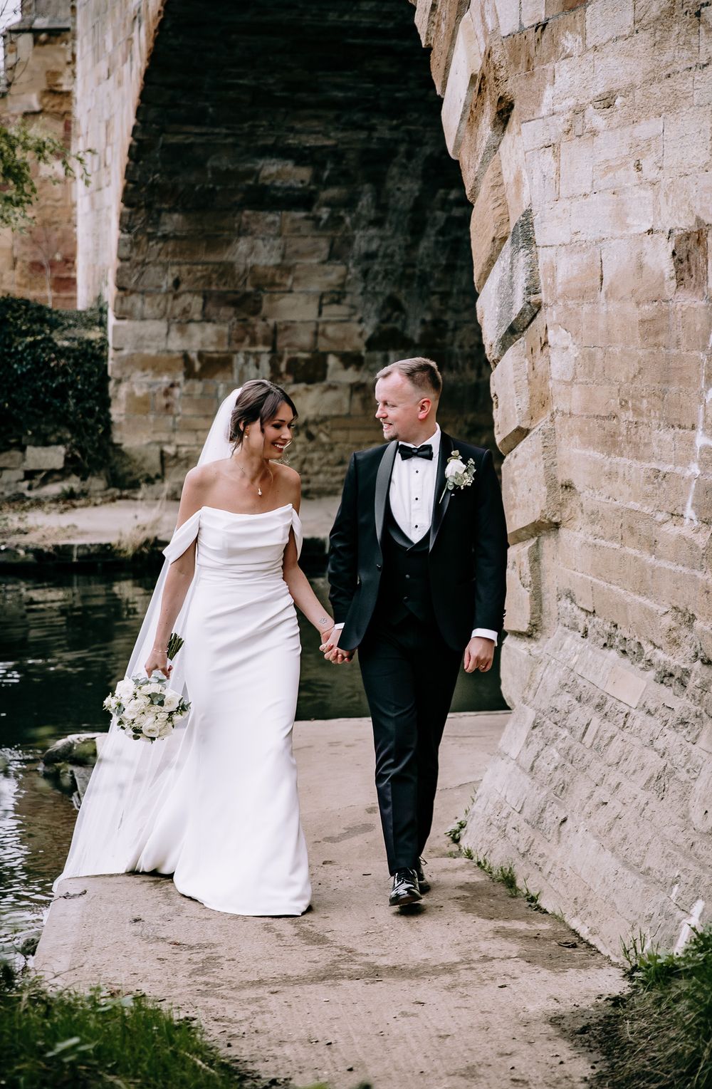 Wedding couple walking along stone walls and archways in an ancient castle setting.