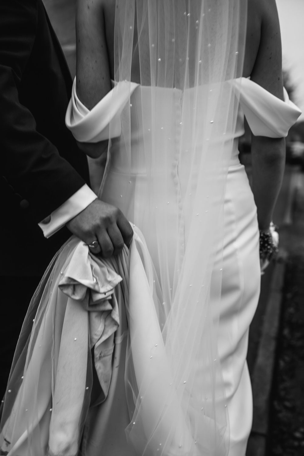 Black and white detail of bride's elegant fitted wedding dress with off-shoulder design.