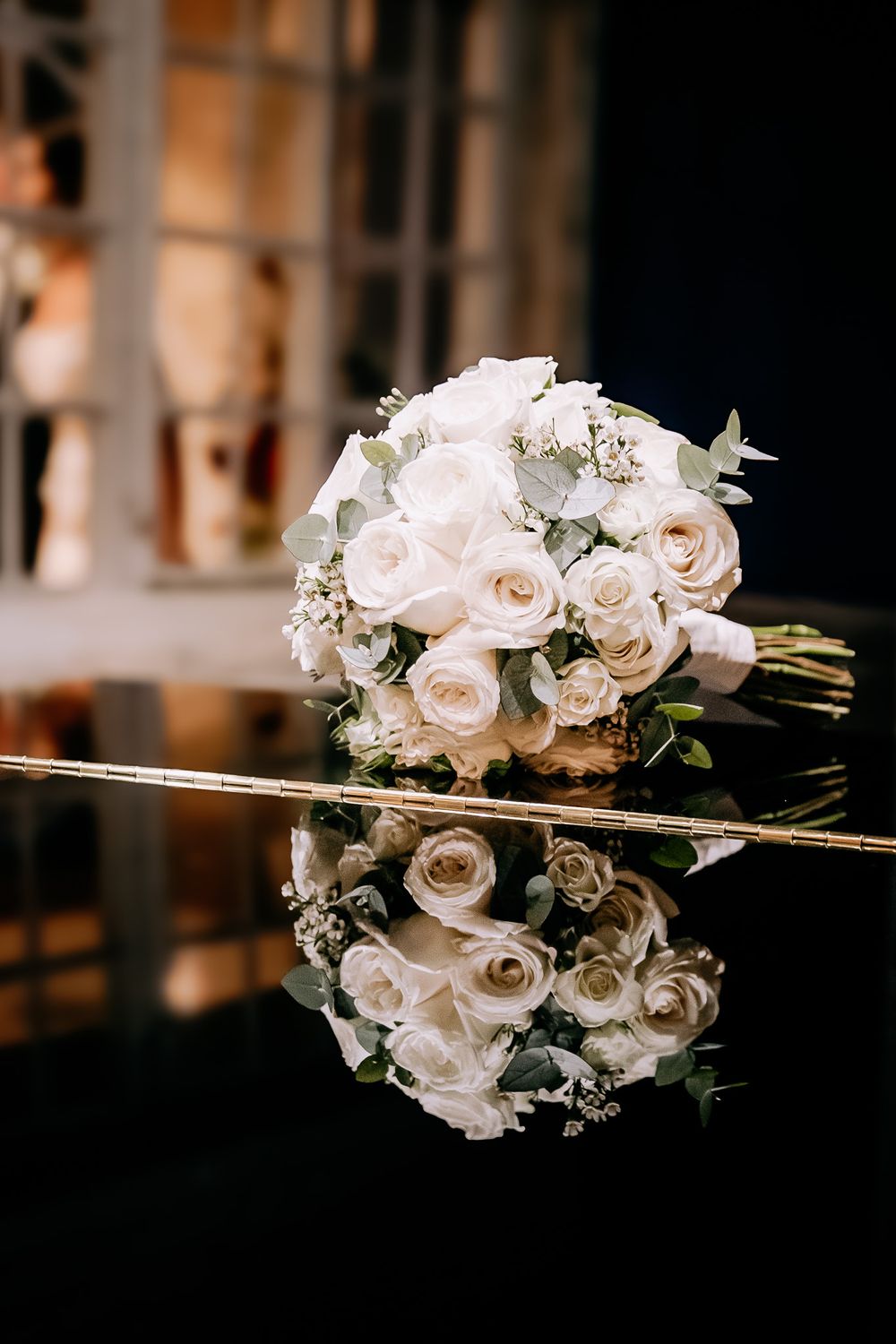 White rose wedding bouquet reflected on glossy dark surface.