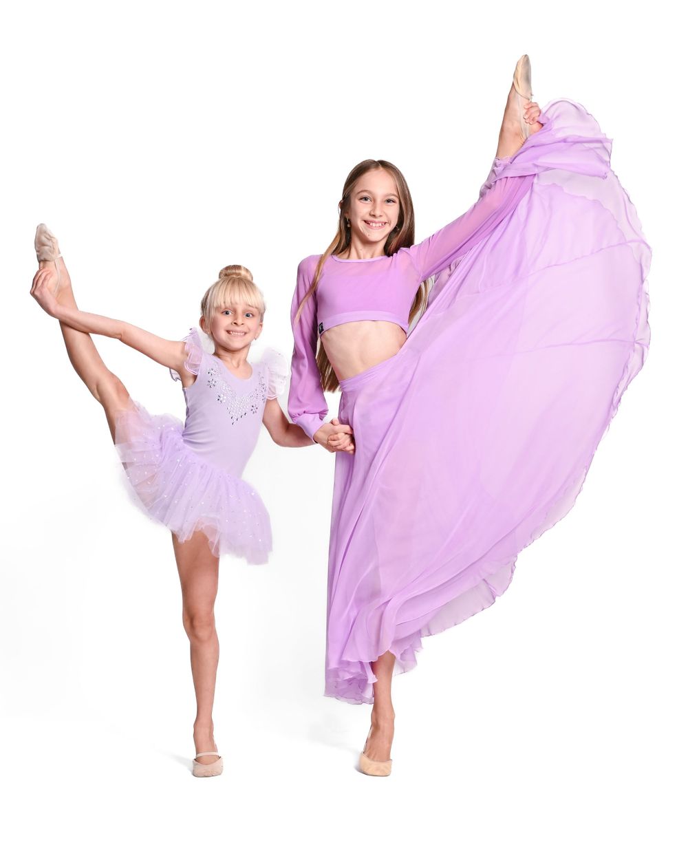 Two dancers in purple outfits strike graceful ballet poses against a white backdrop.