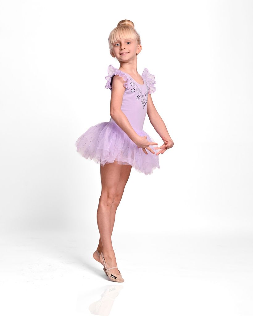 Young dancer in lavender tutu and ballet slippers poses gracefully in a traditional ballet position against white background.