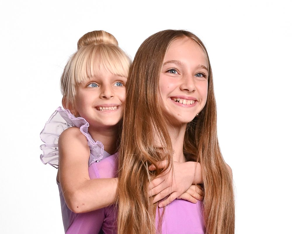 Two young friends in purple outfits pose together with bright smiles against a white background.