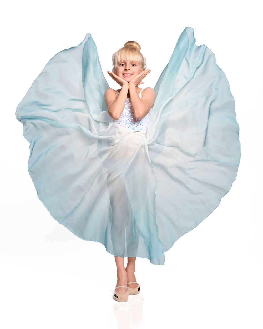 Dancer in flowing light blue dress twirls gracefully against white background creating a circular silhouette.
