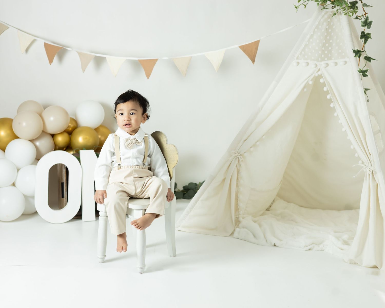 White teepee tent decorated with balloons and bunting creates a cozy reading nook in a bright nursery setting.