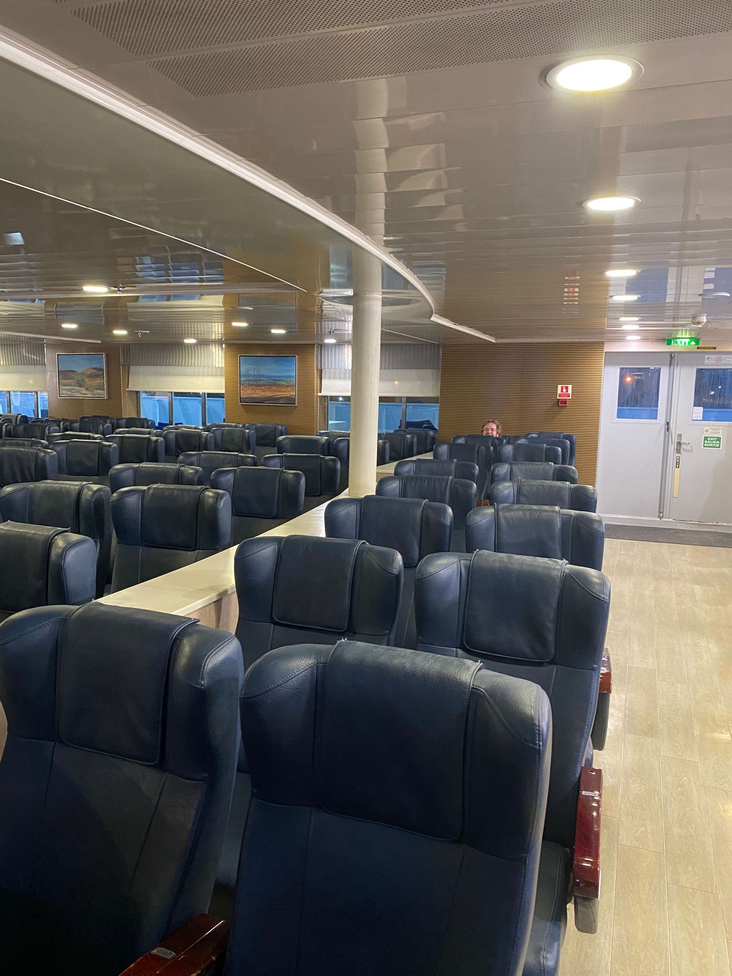 Interior view of a passenger ferry cabin showing rows of blue upholstered seats in an empty seating area.