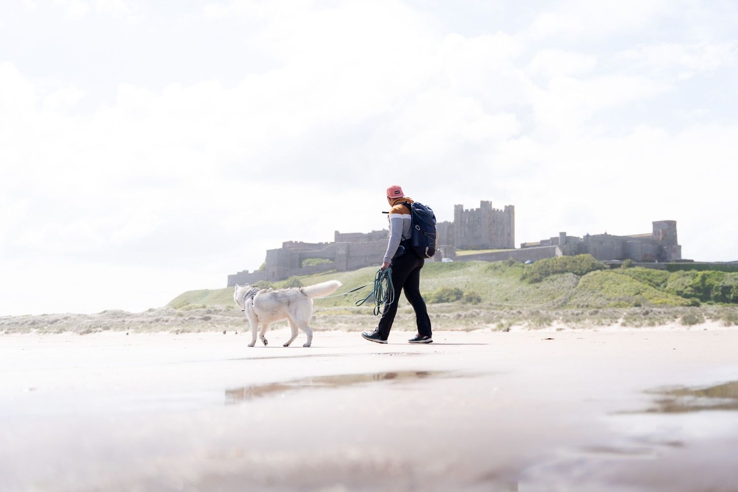 Homme avec son chien sur la plage devant le château de Bamburgh