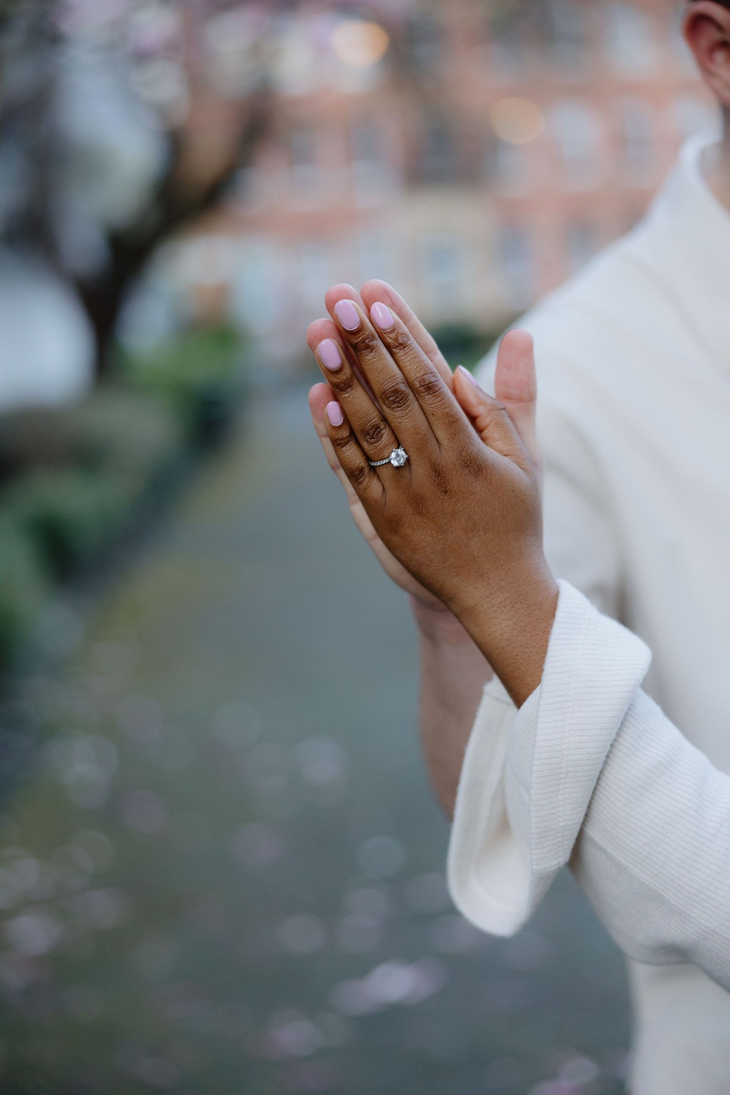 Close-up shots of hands wearing a white sweater showing off an engagement ring with a blurred background.
