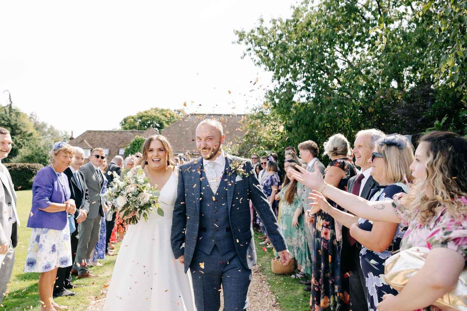 Wedding guests toss confetti and flower petals at a joyful outdoor celebration.