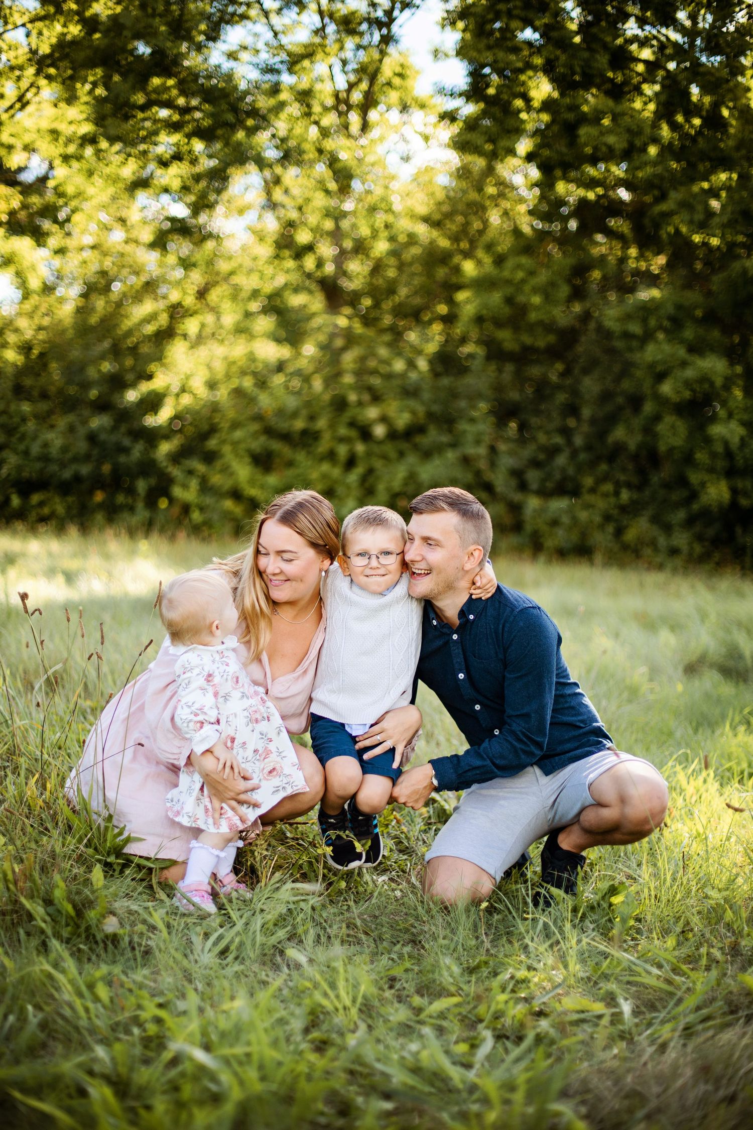 En familj sitter tillsammans på en solbelyst äng med högt gräs och träd under gyllene timmen.