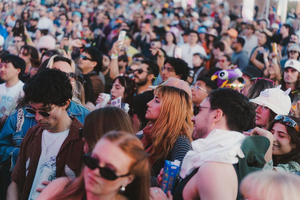 A large crowd of festival attendees watches a performance at an outdoor music event during daytime.