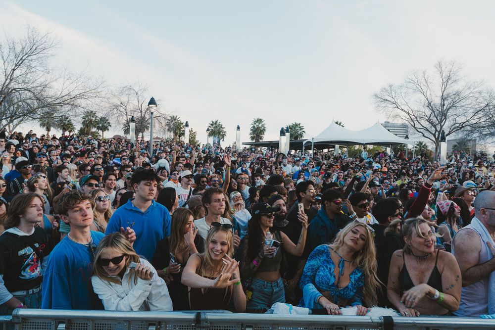 A large crowd of festival attendees gathers outdoors during a live music event.