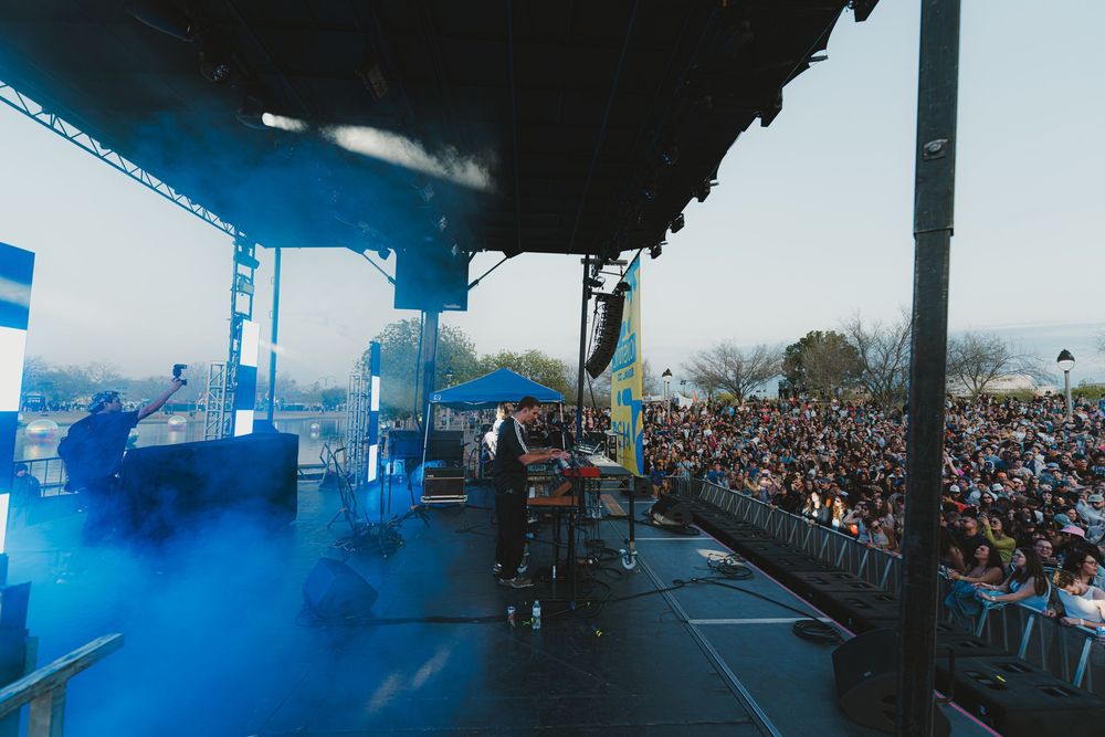 A concert stage with blue lighting and a large crowd of fans visible from the performer's perspective.