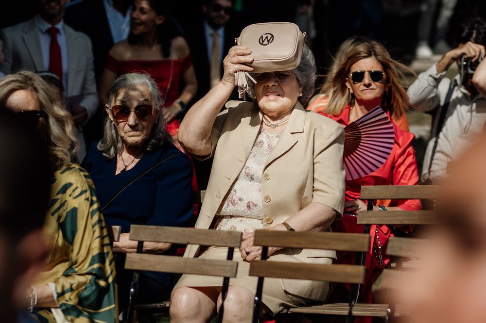 A crowd of spectators wearing sunglasses sits in outdoor stadium seating on a sunny day.