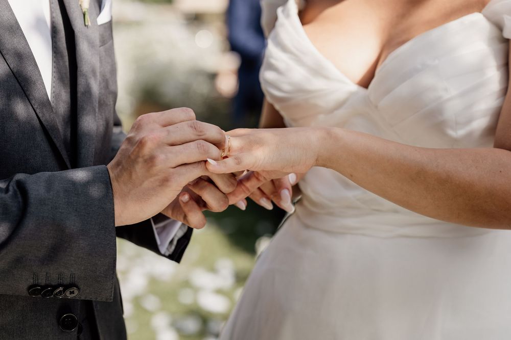 Close up shot of hands exchanging wedding rings during an outdoor ceremony.