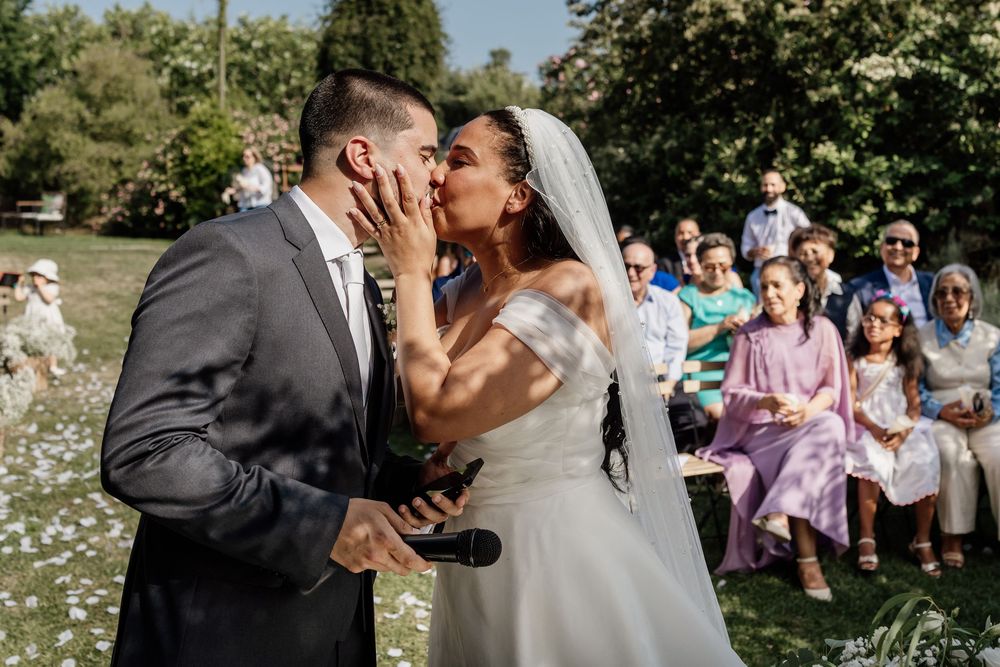 A couple shares their first kiss as newlyweds during an outdoor garden wedding ceremony while guests look on.
