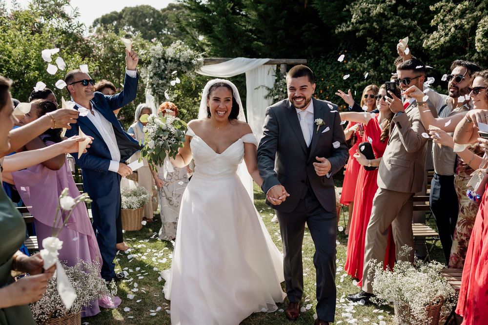 Wedding party celebration outdoors with guests throwing flower petals as newlyweds walk through.