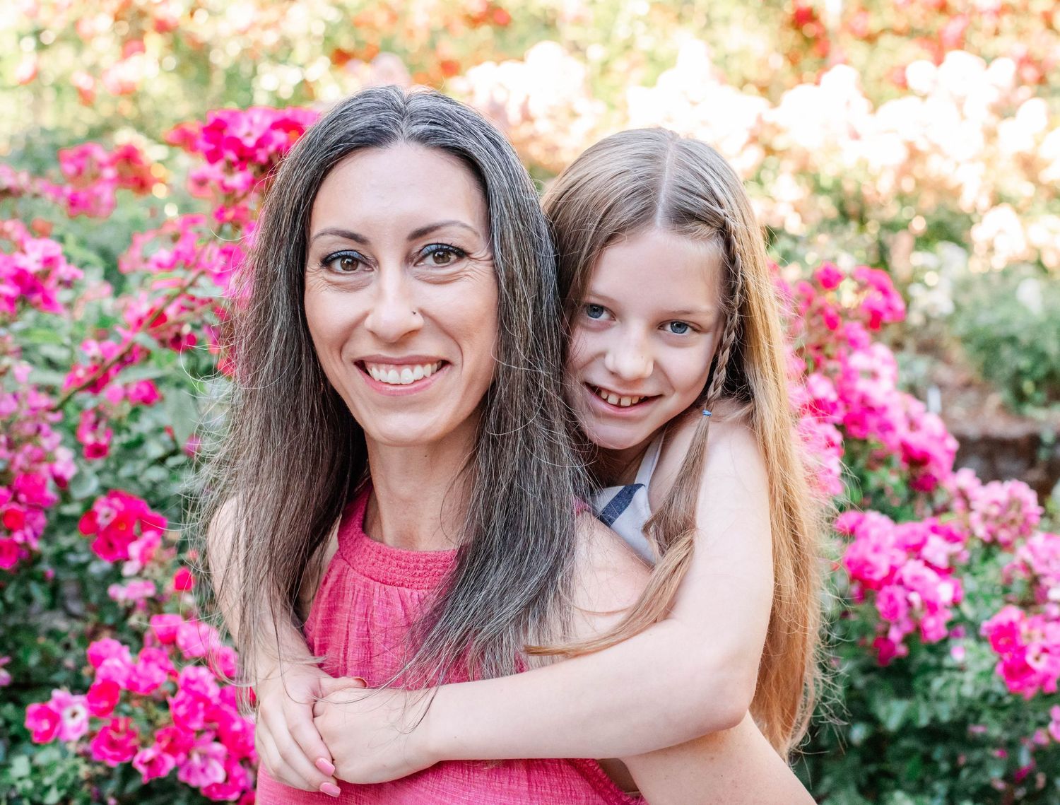 Two people share a joyful embrace in a garden filled with blooming pink flowers on a sunny day.