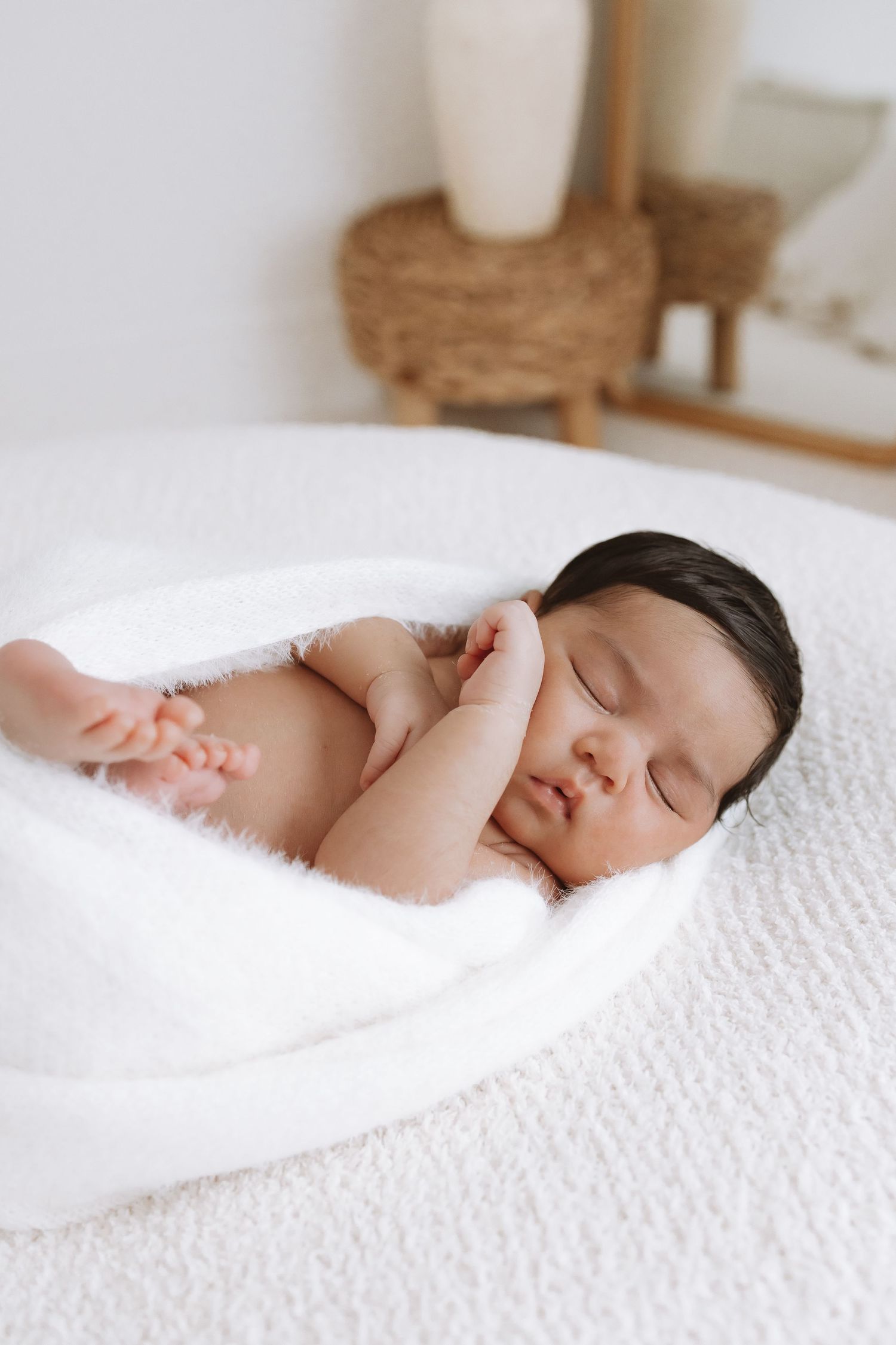 Sleeping newborn baby nestled in soft white bedding and blankets during peaceful nap time.