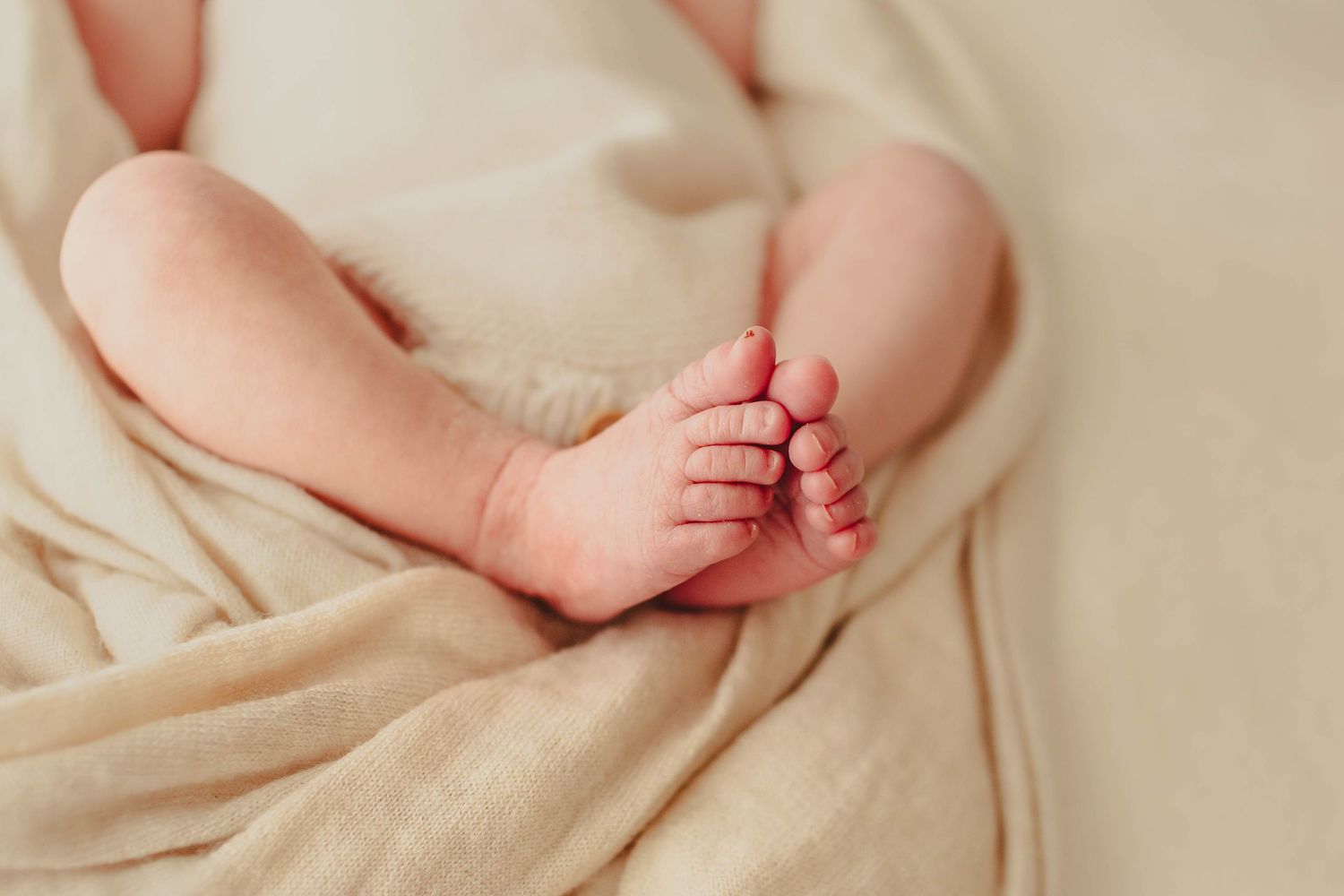 Peaceful newborn baby sleeping wrapped in a soft cream knit blanket with tiny hands tucked under chin.