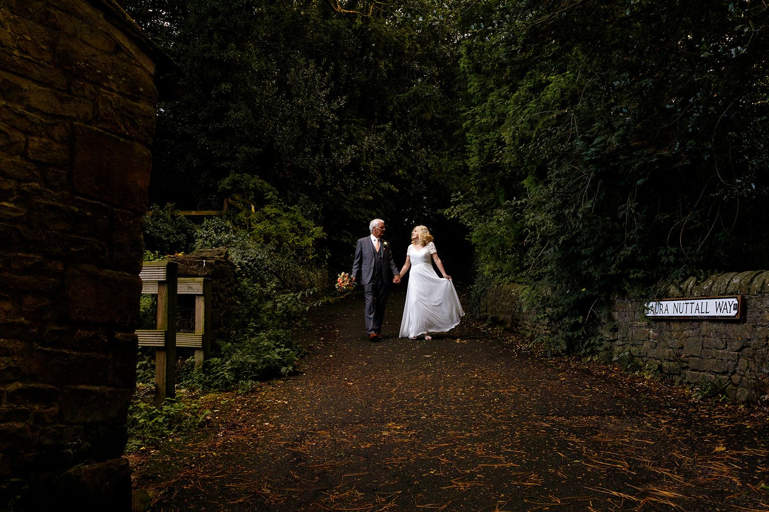 A bride and groom walk down a path surrounded by lush greenery in an outdoor wedding setting.