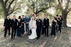 Elegant wedding party poses under oak trees with bride in white gown and groomsmen in black suits.