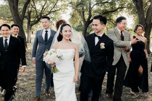 Bride laughing with groom and wedding party during candid outdoor walk at tree-lined venue.