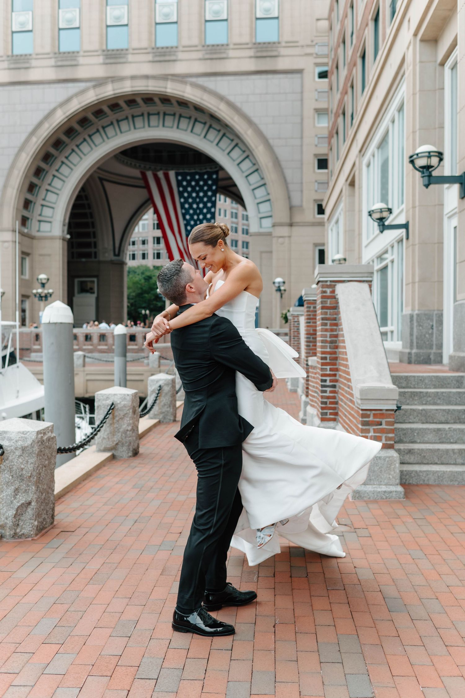 Romantic couple in formal attire dances and dips on brick courtyard with historic building facade in background.