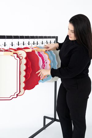 A person in black clothing arranges colorful paper sculptures on a white wall-mounted display system.