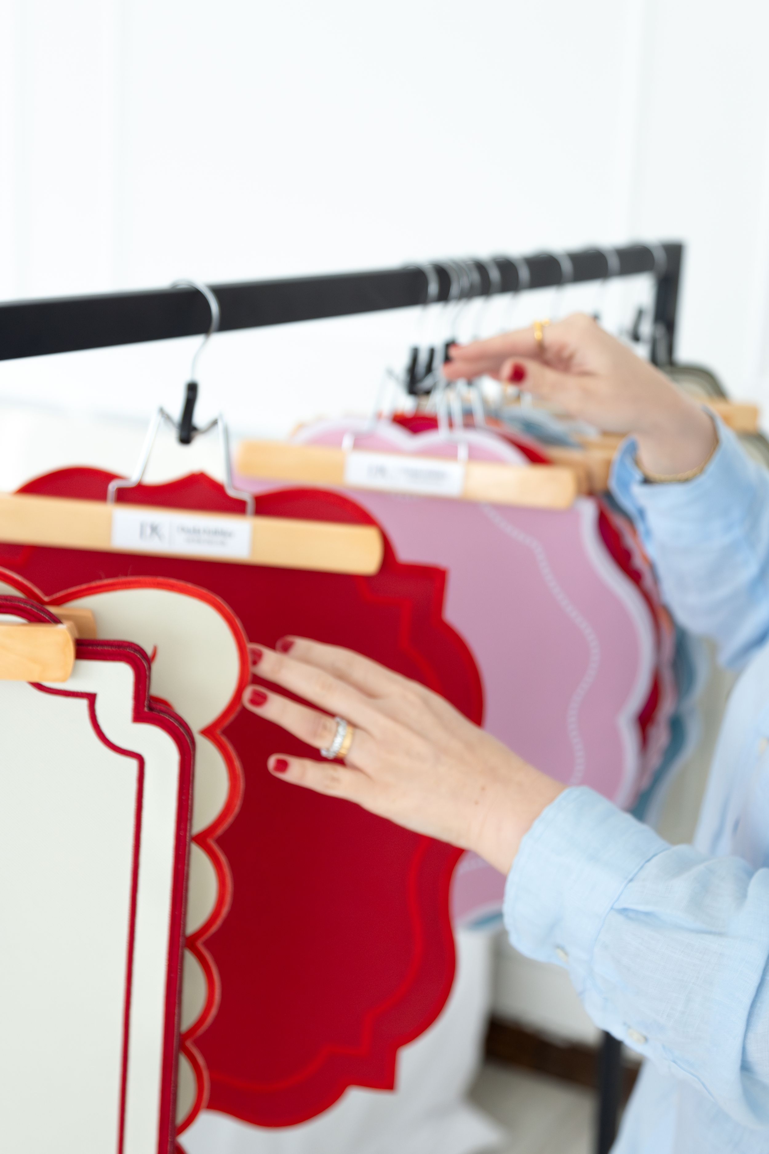 Hands carefully arranging red and pink garments on clothing hangers in a retail store display.