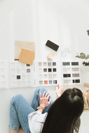 Designer sitting on floor reviewing color swatches and material samples laid out on white surface for interior design project.