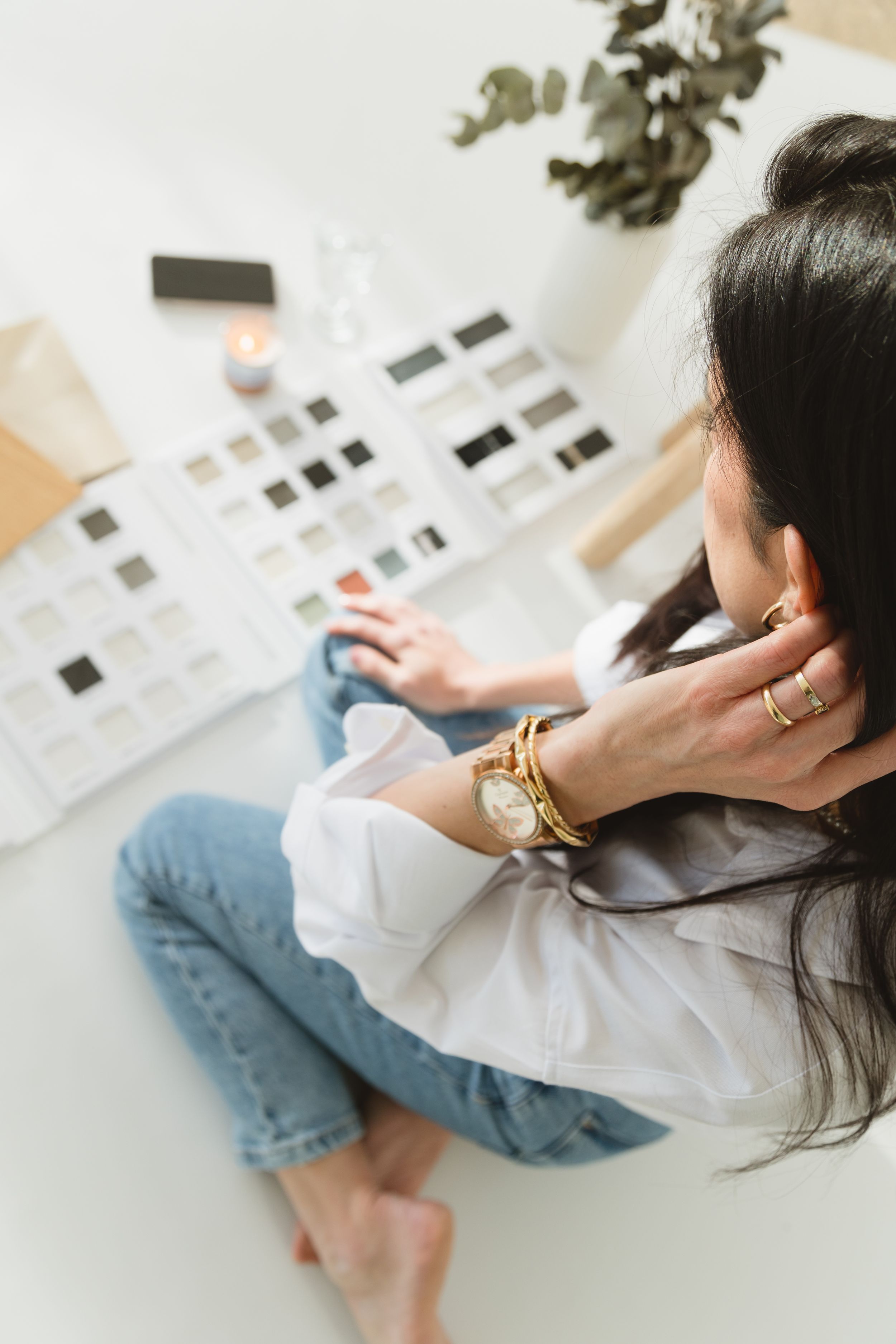 Person in white shirt and jeans sits on floor while looking at black and white photo prints laid out on surface.