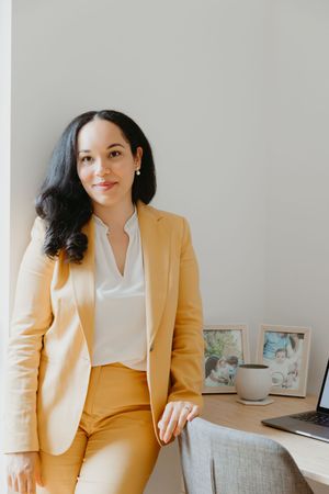 Professional wearing a stylish yellow pantsuit and white blouse poses in a minimalist interior setting.