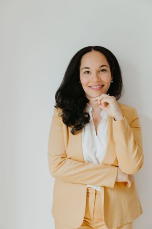 Professional wearing a light yellow blazer and white shirt poses confidently against a white background.