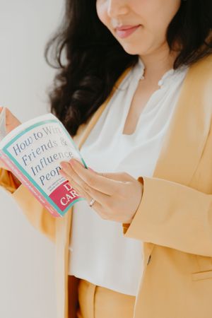 Person in yellow suit jacket holds colorful business cards while standing against white wall.