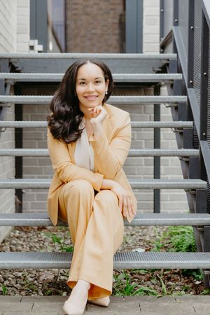 Individual in yellow business suit sits casually on outdoor metal bleachers.