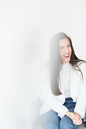 A person wearing a white top and blue jeans poses against a white background in a casual photoshoot series.