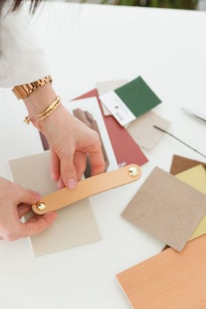 Hands with gold jewelry arrange colorful paper swatches and samples on a white surface.