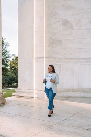 A woman in casual clothing walks near a large, white marble building with columns.