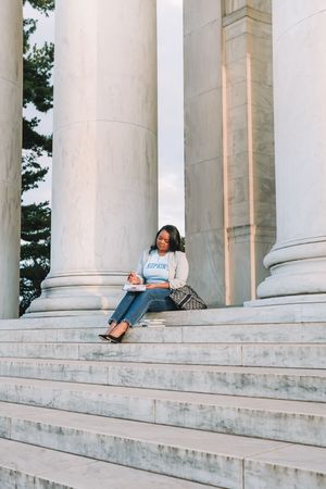 A woman sits on the steps of a grand, columned building, enjoying a moment of relaxation.
