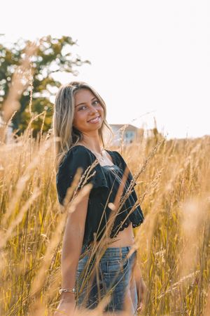 A smiling young woman stands in a field of golden wheat, surrounded by nature and sunlight.