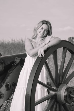 A smiling woman posing next to an old cannon in a grassy field.