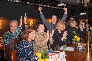 Excited crowd cheering with raised arms at a lively bar gathering.